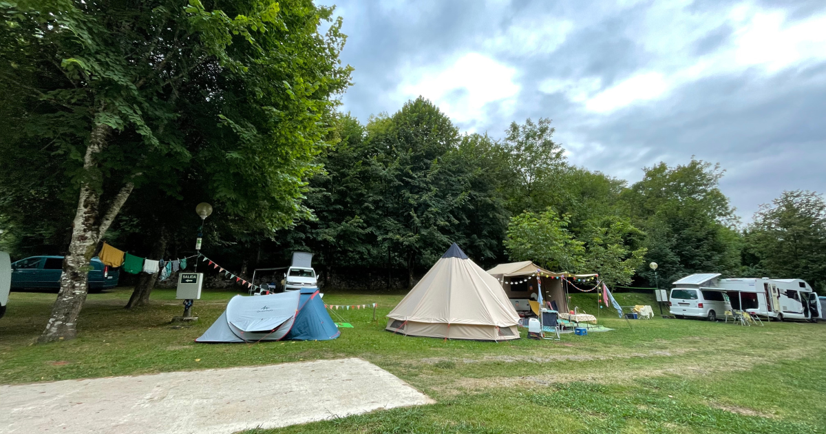 campo verde con tiendas de campaña y campers en camping de Naranjo de Bulnes.