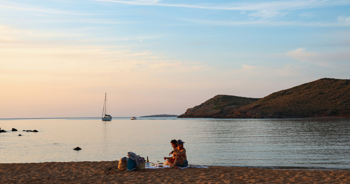 Pareja sentada en una playa de Menorca durante el atardecer